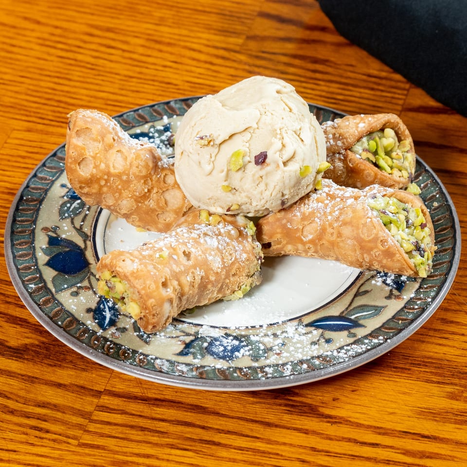 Pistachio-filled cannoli dusted with powdered sugar surround a scoop of ice cream on a decorative plate.
