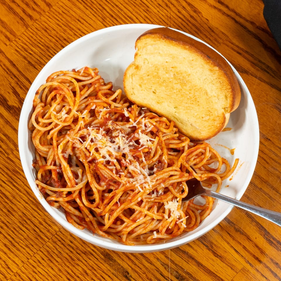 Plate of spaghetti with tomato sauce and melted cheese, served with garlic bread on a wooden restaurant table.