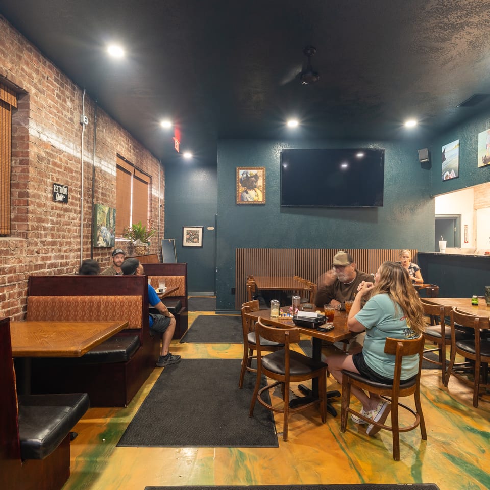 Interior of a lively restaurant with exposed brick walls, booth seating, wooden tables, framed artwork, and diners.