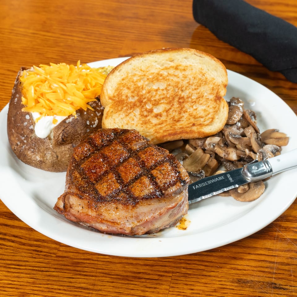 Grilled steak with sautéed mushrooms, cheesy baked potato, and toasted bread served on a white plate.