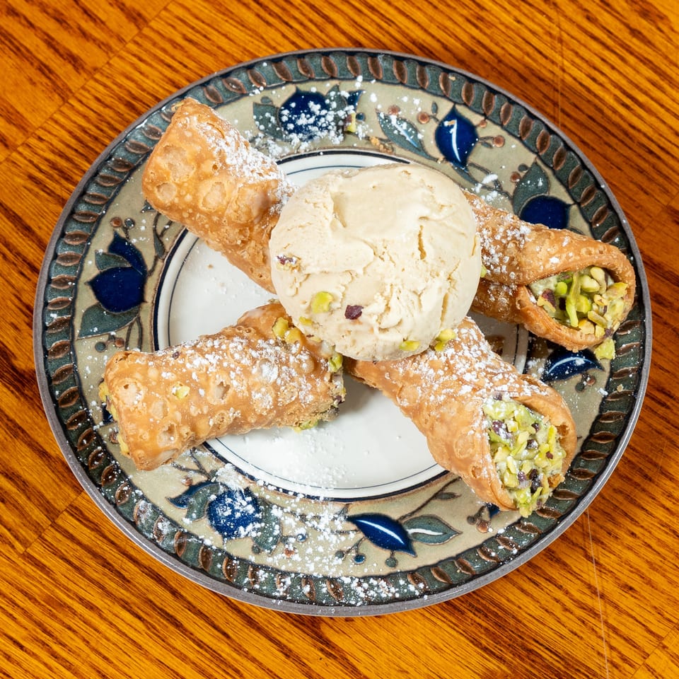 Pistachio-filled pastries dusted with powdered sugar surround a scoop of vanilla ice cream on a decorative plate.
